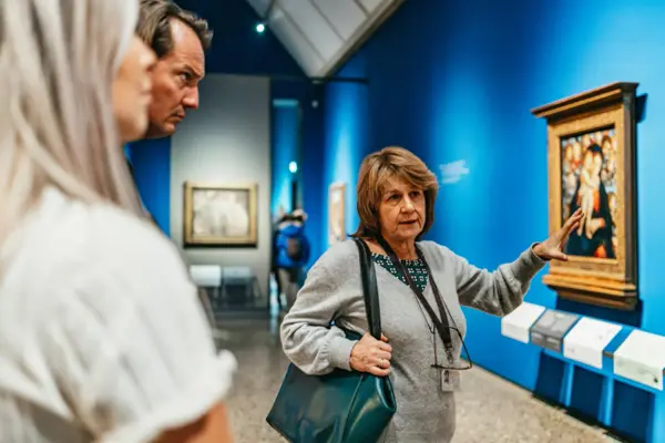 A guide and visitors in front of a painting in the gallery