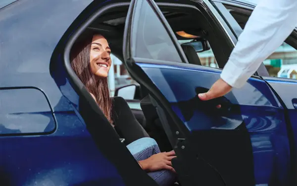 A driver holding the car door open for a passenger